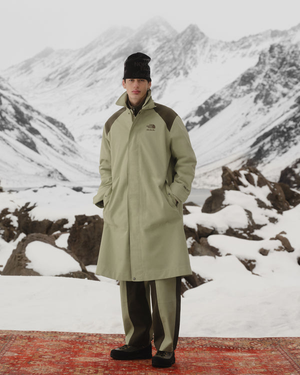 Someone in an ALD/The North Face GORE-TEX Trench Coat stands on a red rug with snowy mountains behind.