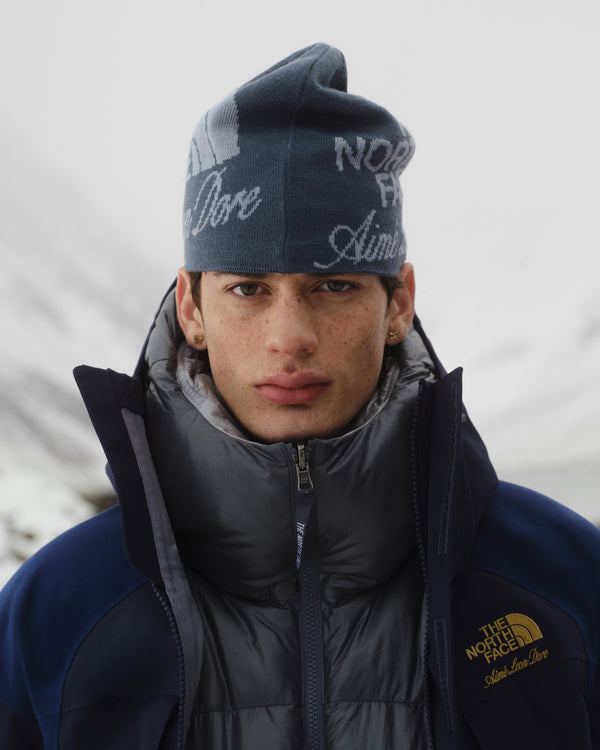 A young man wears an ALD / The North Face Jacquard Beanie outdoors with snowy mountains in the background.