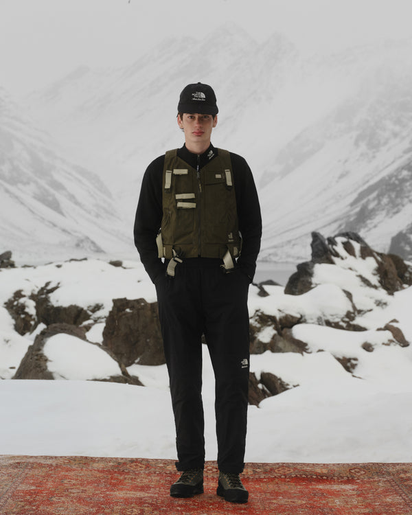 Person wearing the ALD / The North Face Nylon Logo Hat stands on a red rug in a snowy mountain landscape.