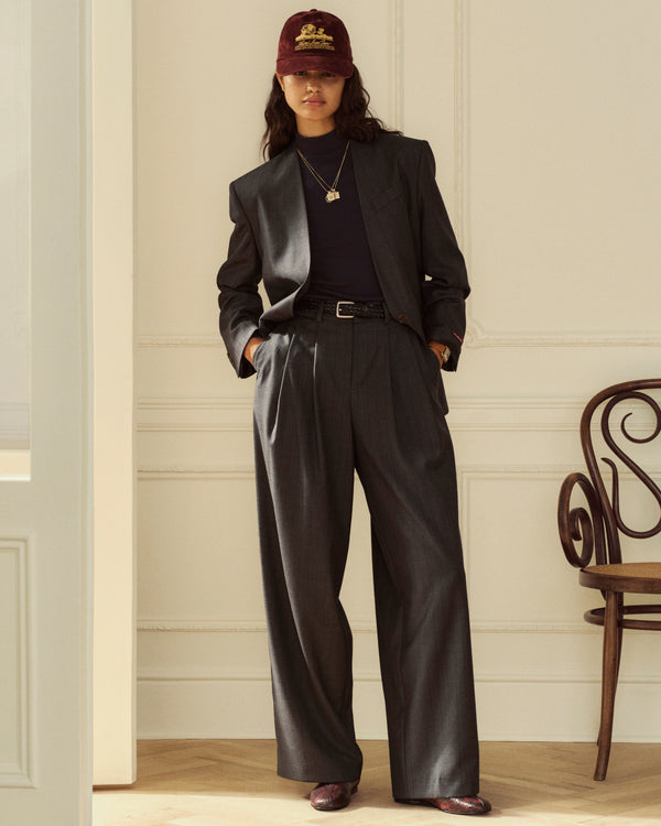 A person wearing a Collarless Striped Blazer with matching wide-leg trousers, a dark turtleneck, and a baseball cap.