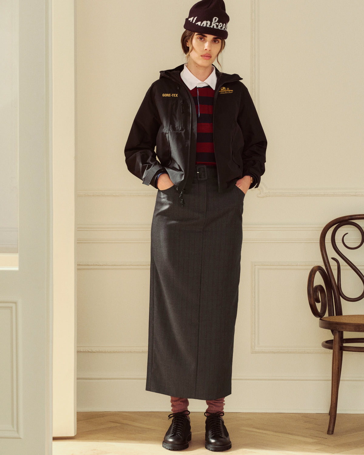 Person wearing a dark hooded jacket, a striped polo shirt, and a Striped Tailored Maxi Skirt.