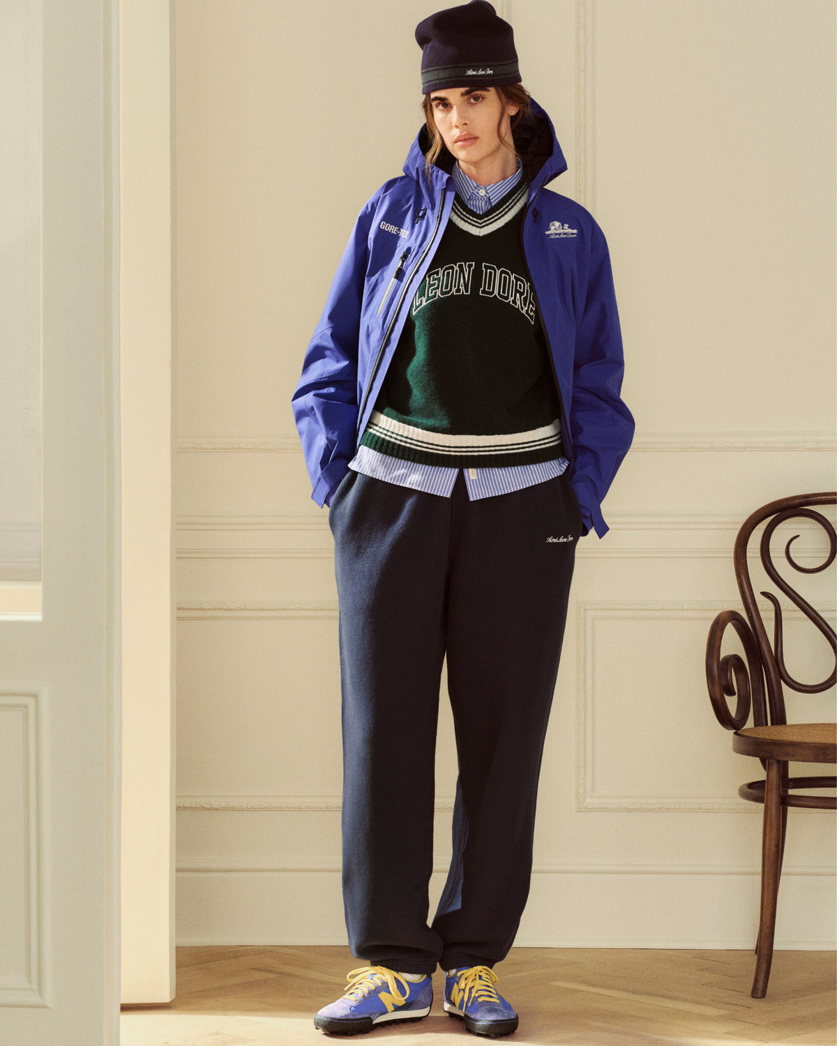 Person wearing a blue hooded jacket over a Striped Button Down Poplin Shirt, green sweater vest, and dark sweatpants.