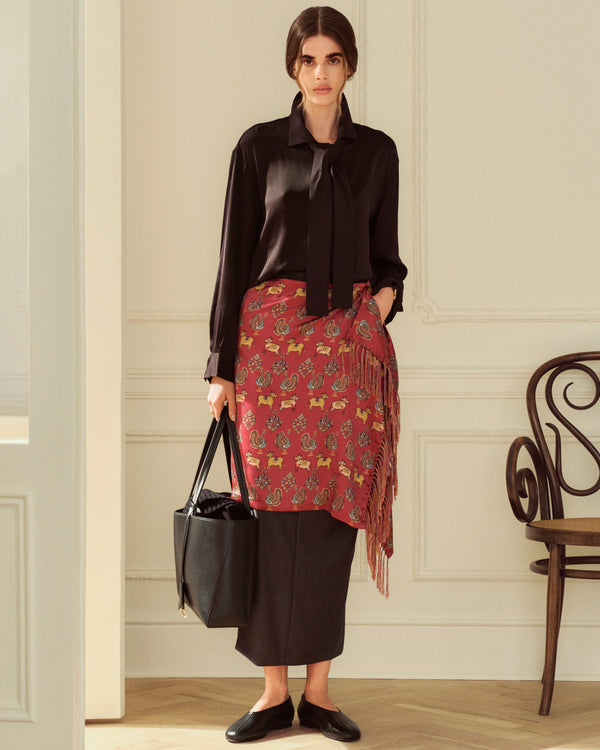 A woman in a black blouse and a patterned wrap skirt holds a black Napa Leather Shoulder Bag.