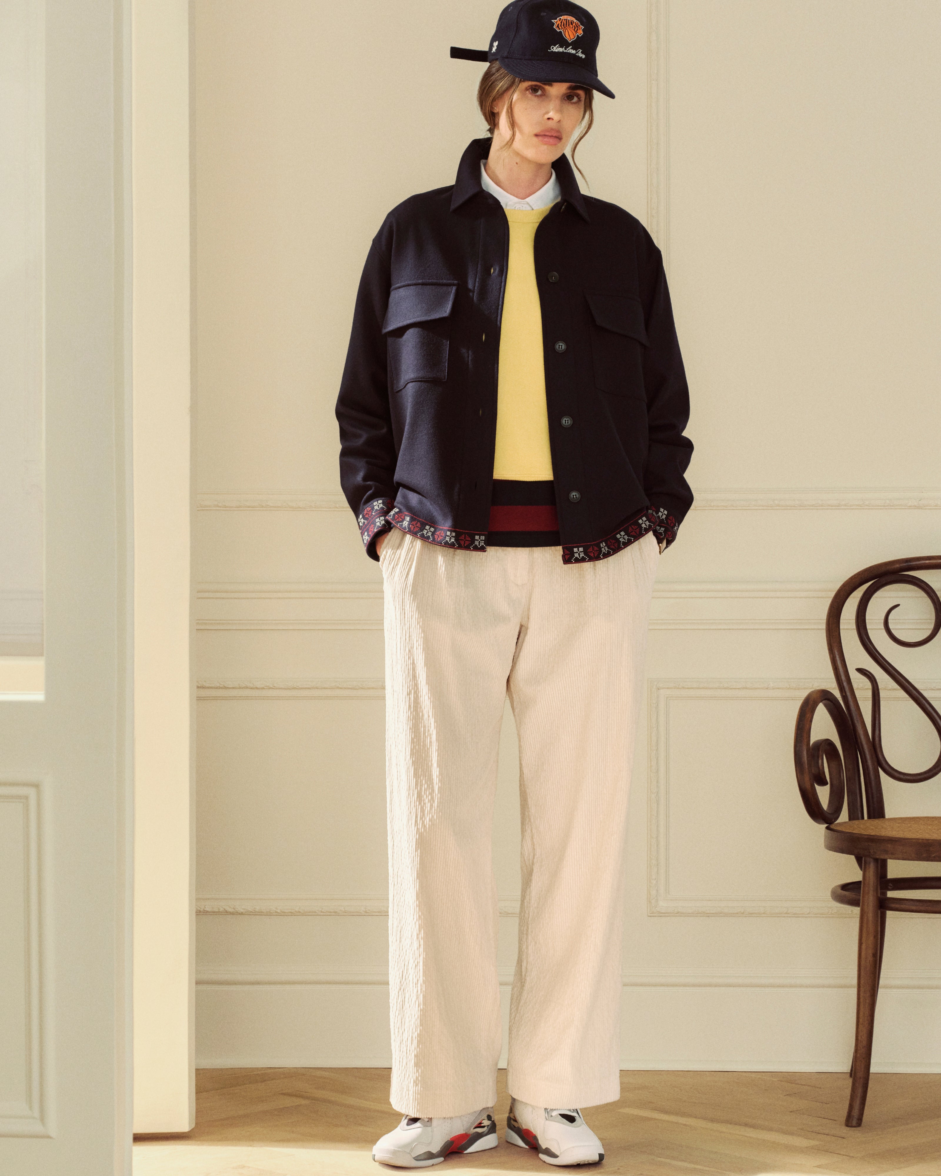 A person wearing a yellow Crest Crewneck Sweatshirt, dark jacket, and light-colored wide-leg trousers.