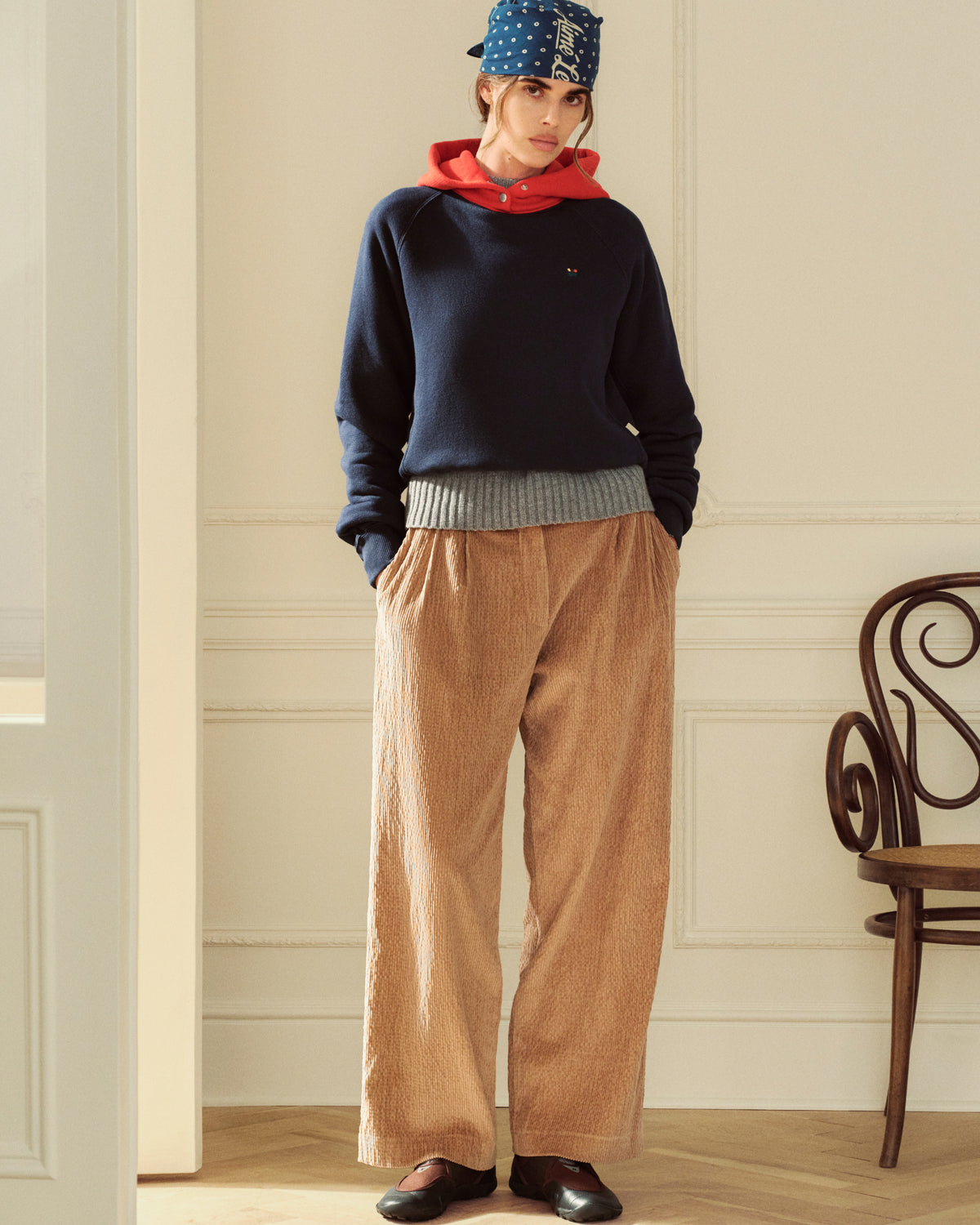 A person wearing a Colorblock Crest Snap Hoodie with a navy body, red hood, grey hem, and tan wide-leg trousers.