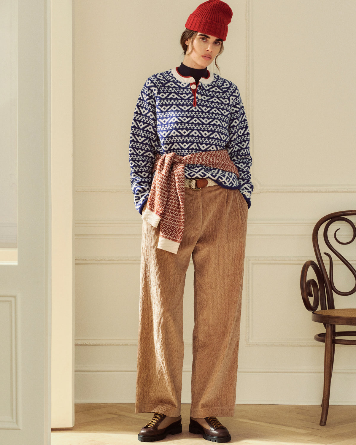 A person wearing a red beanie, a blue and white patterned sweater, and tan Double Pleated Corduroy Trouser.