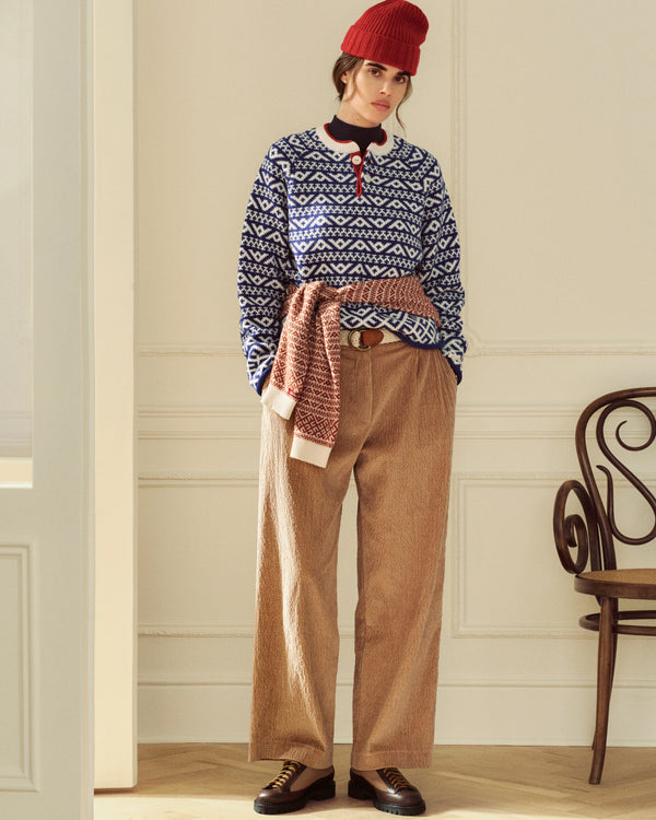 A person wearing a red beanie, a blue and white patterned sweater, and tan Double Pleated Corduroy Trouser.