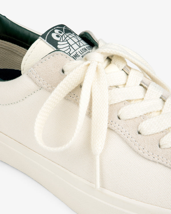 Close-up of ALD / Last Resort AB VM001-LO Canvas white sneaker with cream laces and green tongue logo tag.