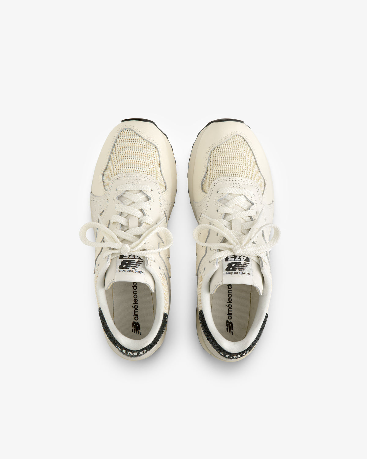 Top view of a pair of ALD / New Balance 475 off-white sneakers with tied laces, side by side on a white background.