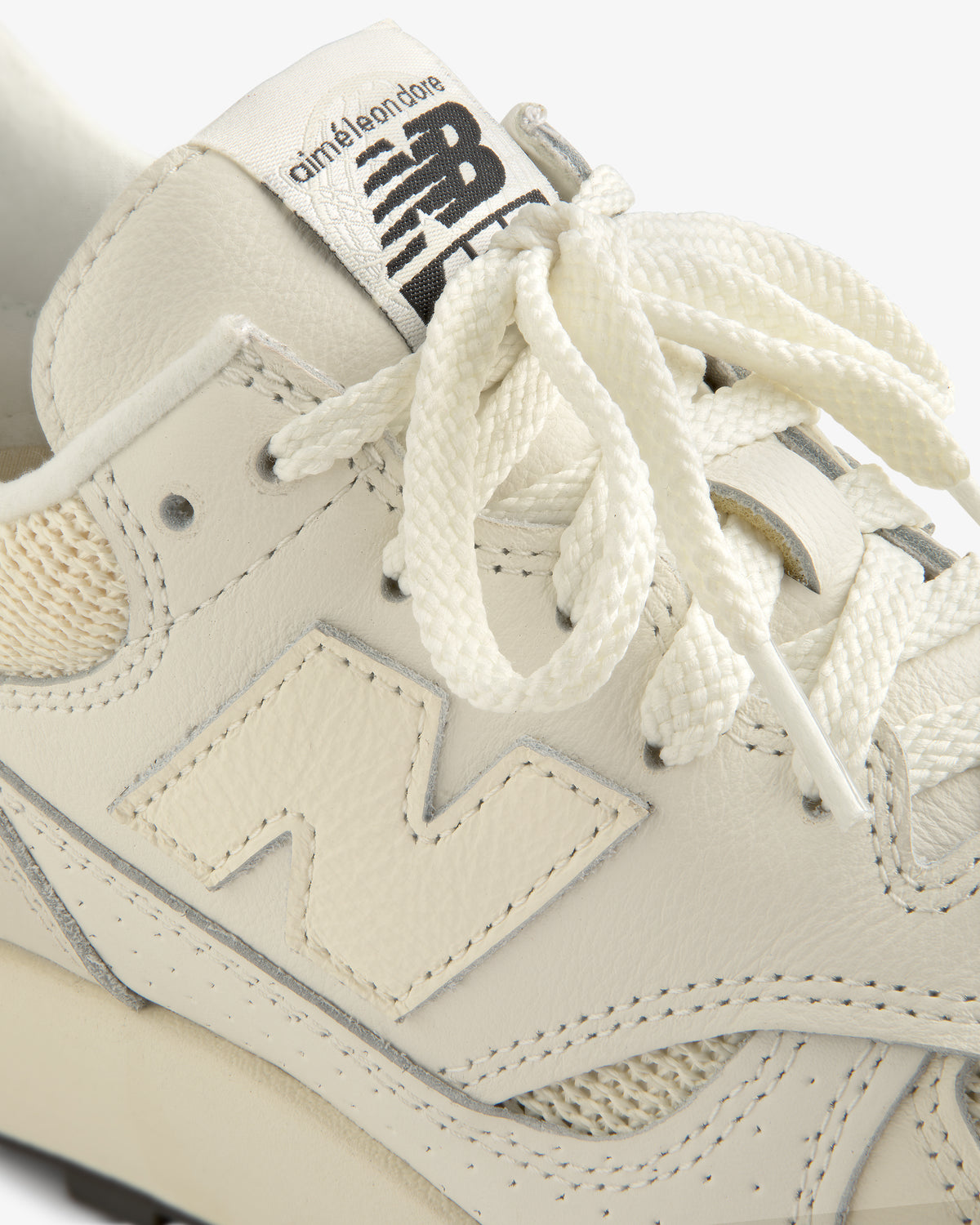 Close-up of a cream New Balance ALD / New Balance 475 sneaker with branding on tongue and logo on side.