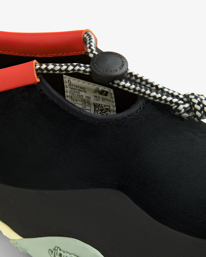 Close-up of the ALD / New Balance MT10T Sport Shoe: black, toggle laces, orange trim, shoe tag inside, Vibram sole logo.