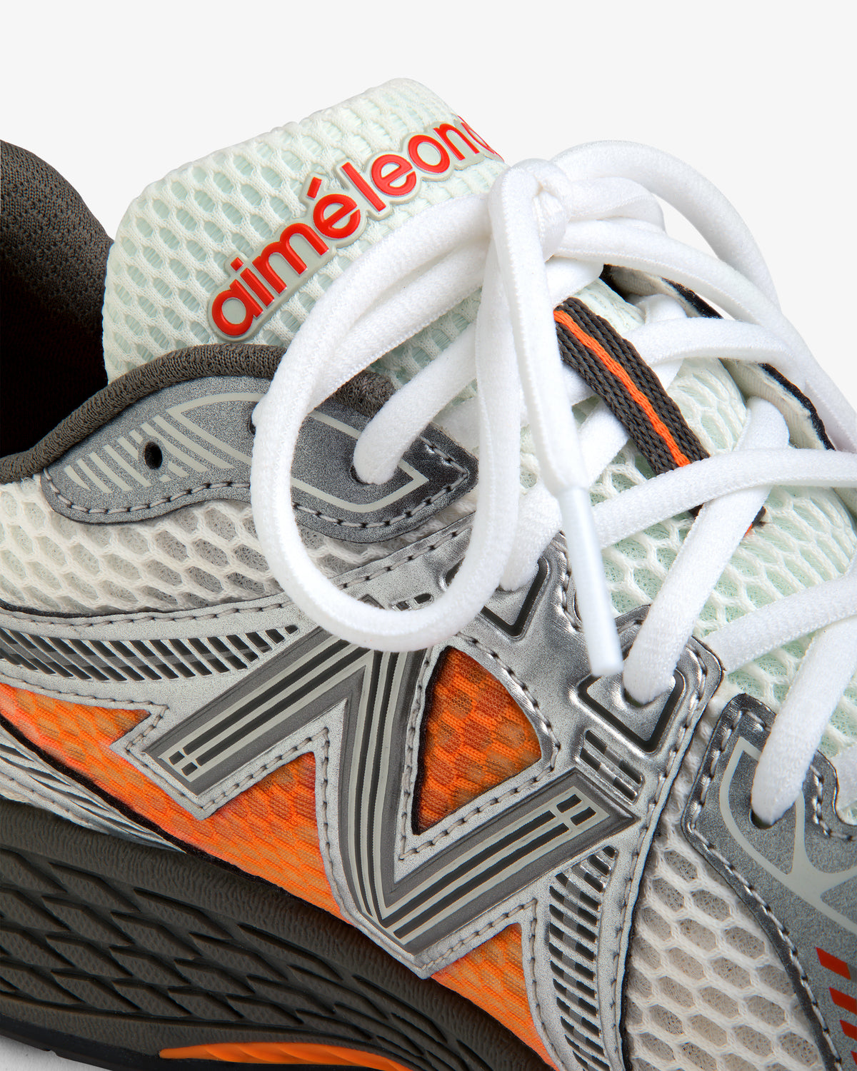 Close-up of ALD / New Balance 860v2 sneaker with mesh texture, orange accents, and red aimé leon d text on tongue.