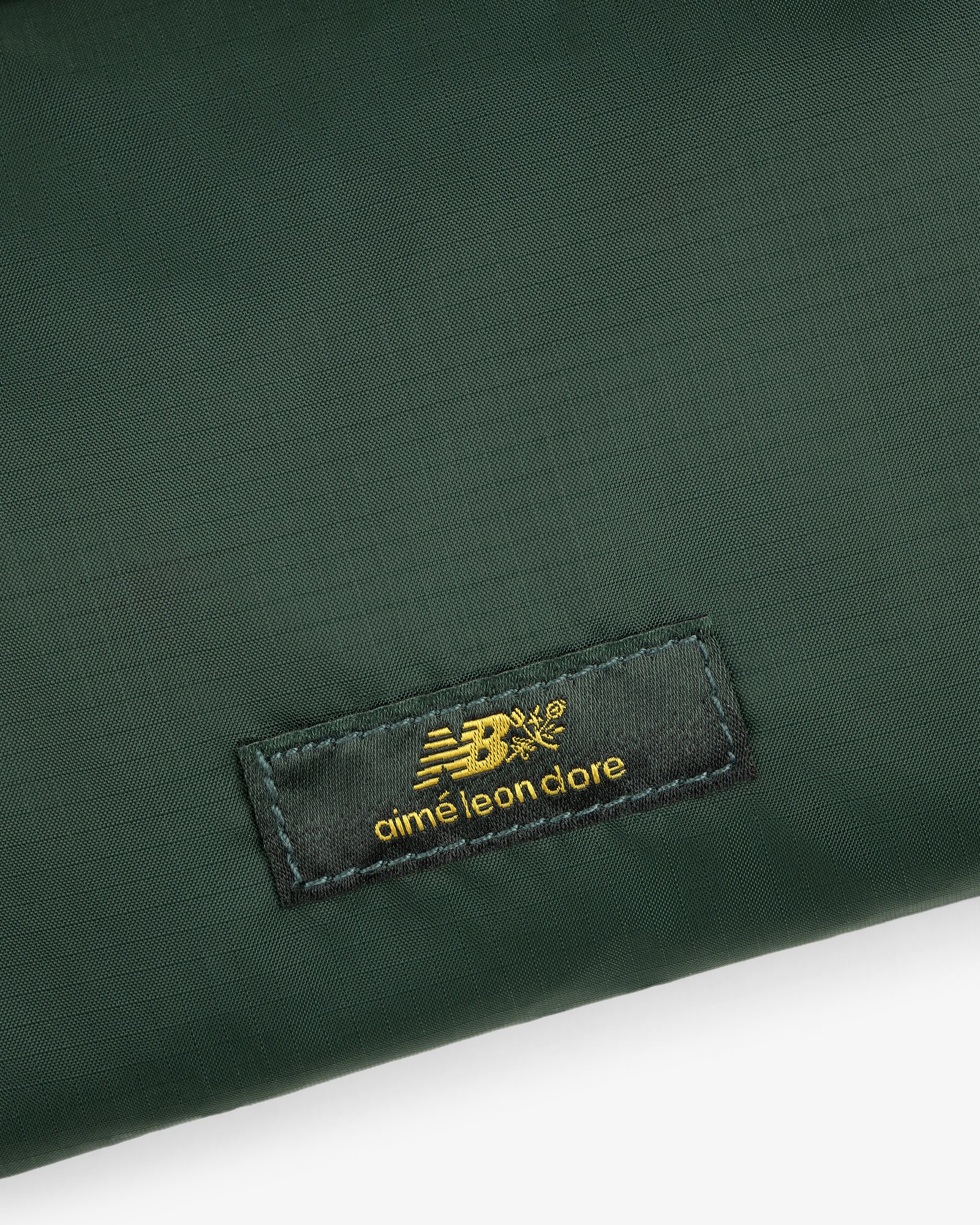 Dark green ALD / New Balance Nylon Sling Pouch with a black label and gold New Balance and Aimé Leon Dore logos.