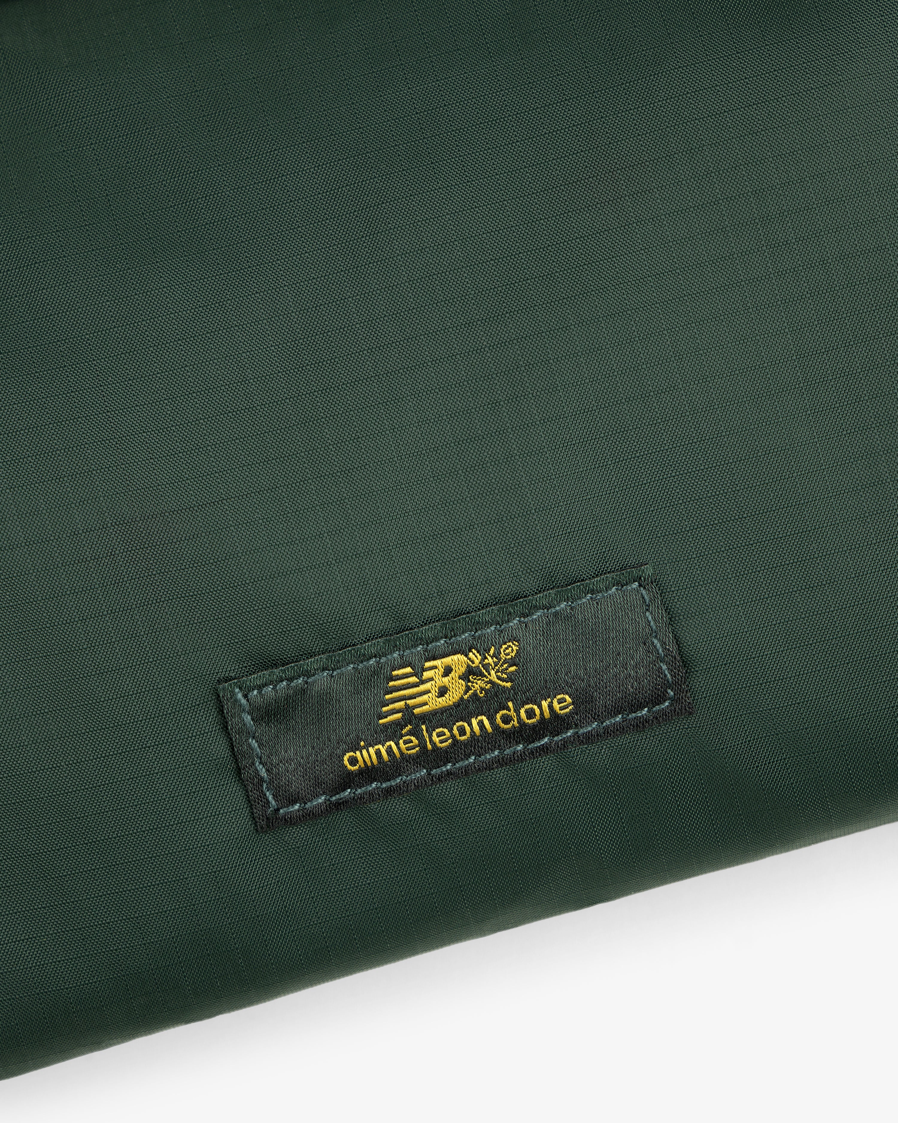 Dark green ALD / New Balance Nylon Sling Pouch with a black label and gold New Balance and Aimé Leon Dore logos.