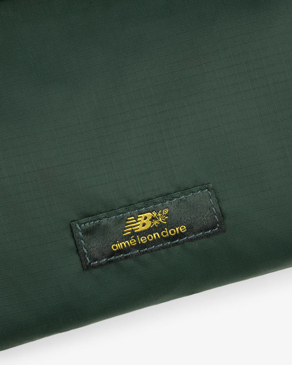 Dark green ALD / New Balance Nylon Sling Pouch with a black label and gold New Balance and Aimé Leon Dore logos.