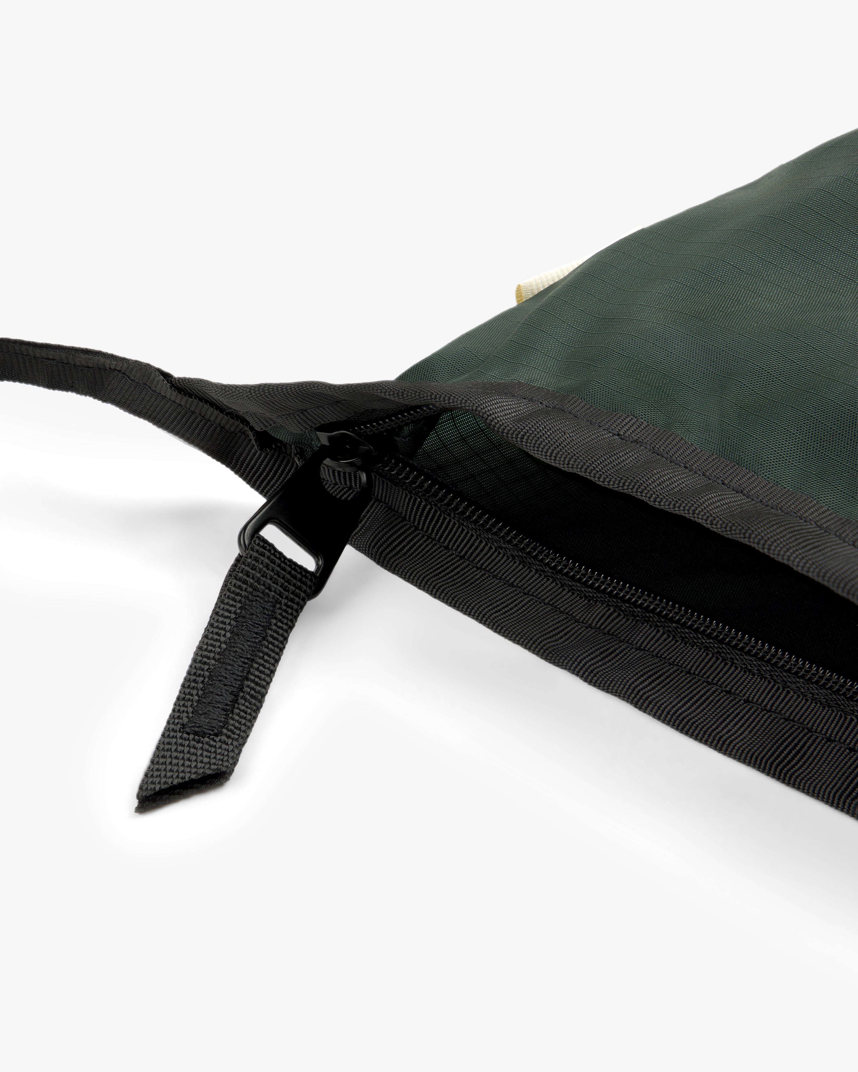 Close-up of the ALD / New Balance Nylon Sling Pouch in green with black zipper and strap on a white background.