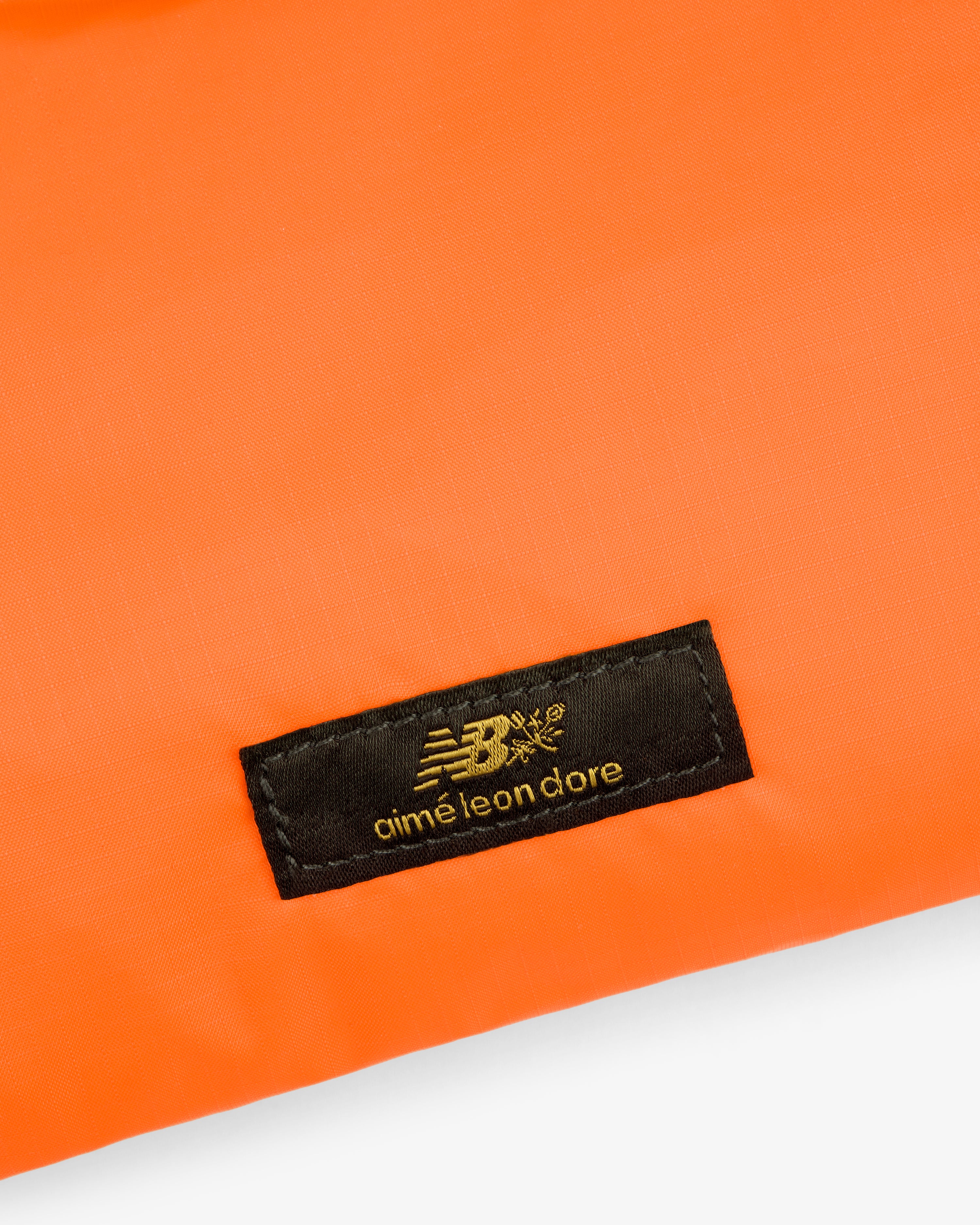 A black ALD / New Balance label on orange nylon fabric sling pouch.