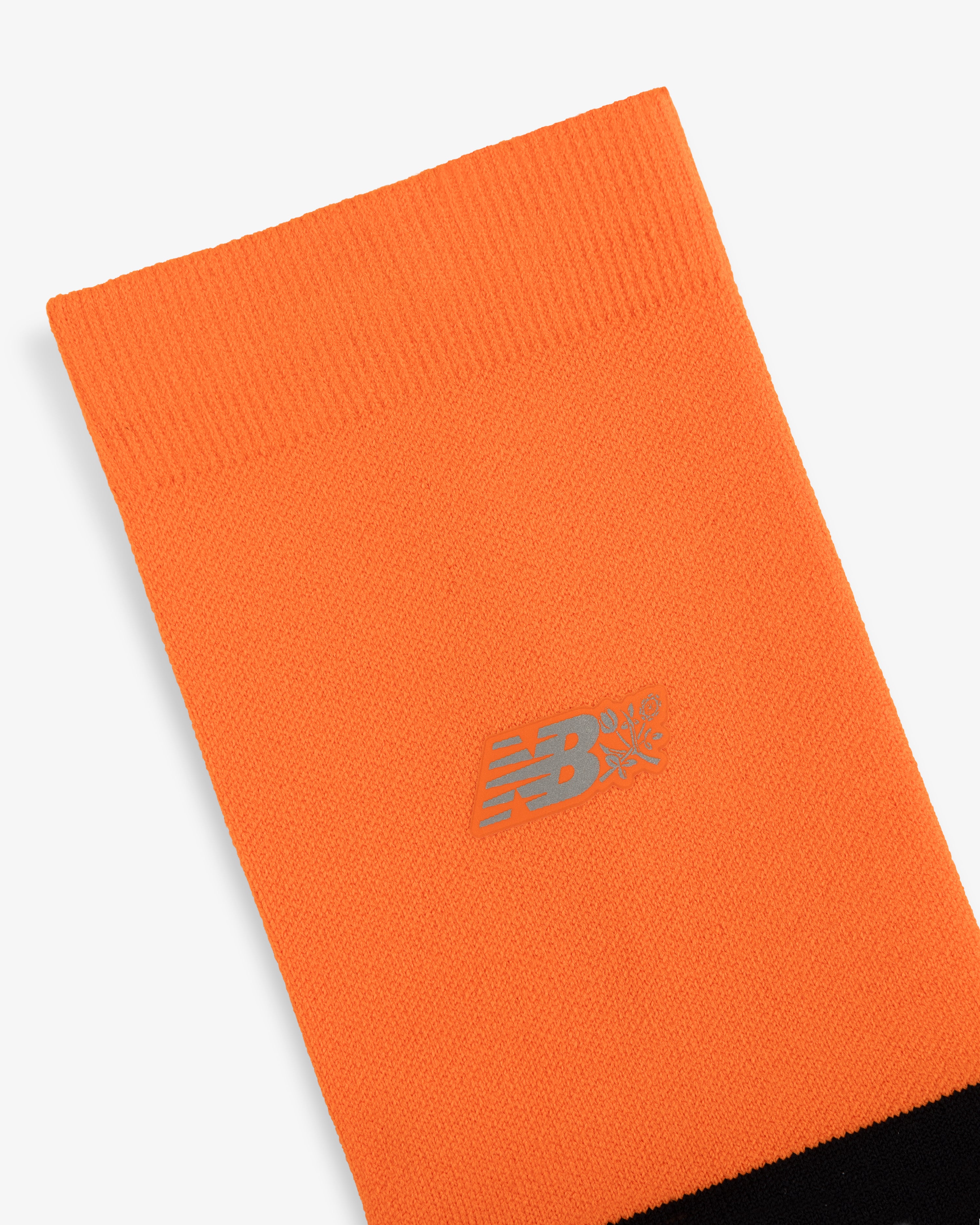 Close-up of an ALD / New Balance Running Crew Sock: orange with a silver logo and black detailing at the bottom edge.