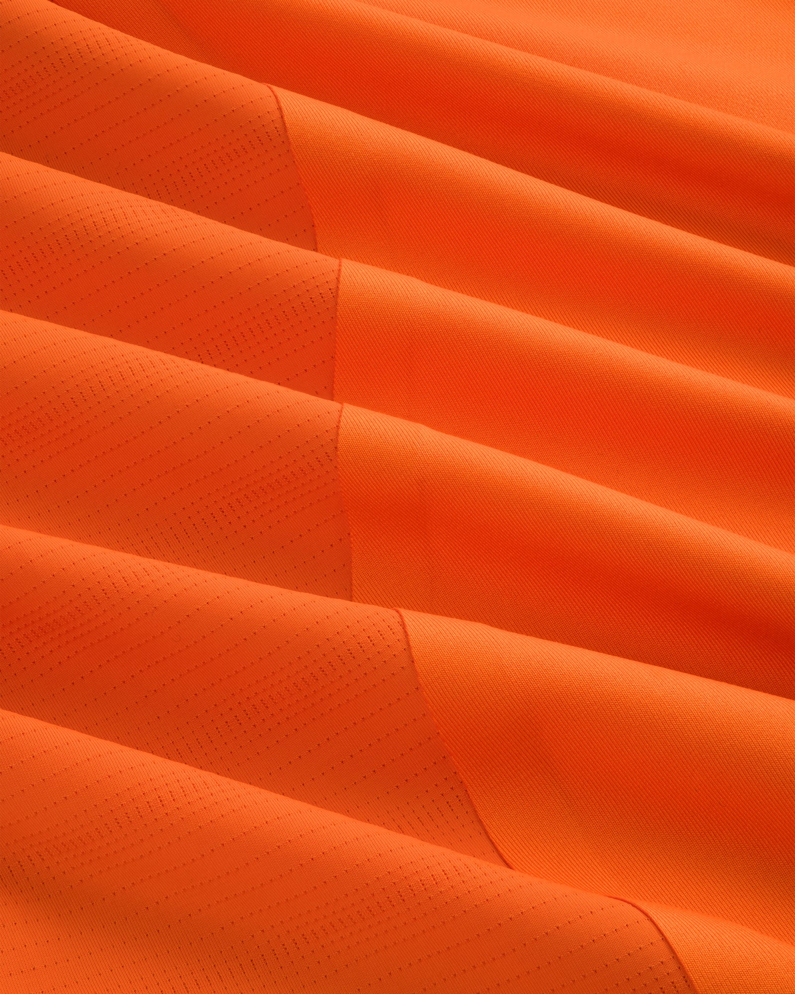Close-up of ALD / New Balance Performance Long-Sleeve Tee in bright orange with subtle dotted texture and diagonal lines.