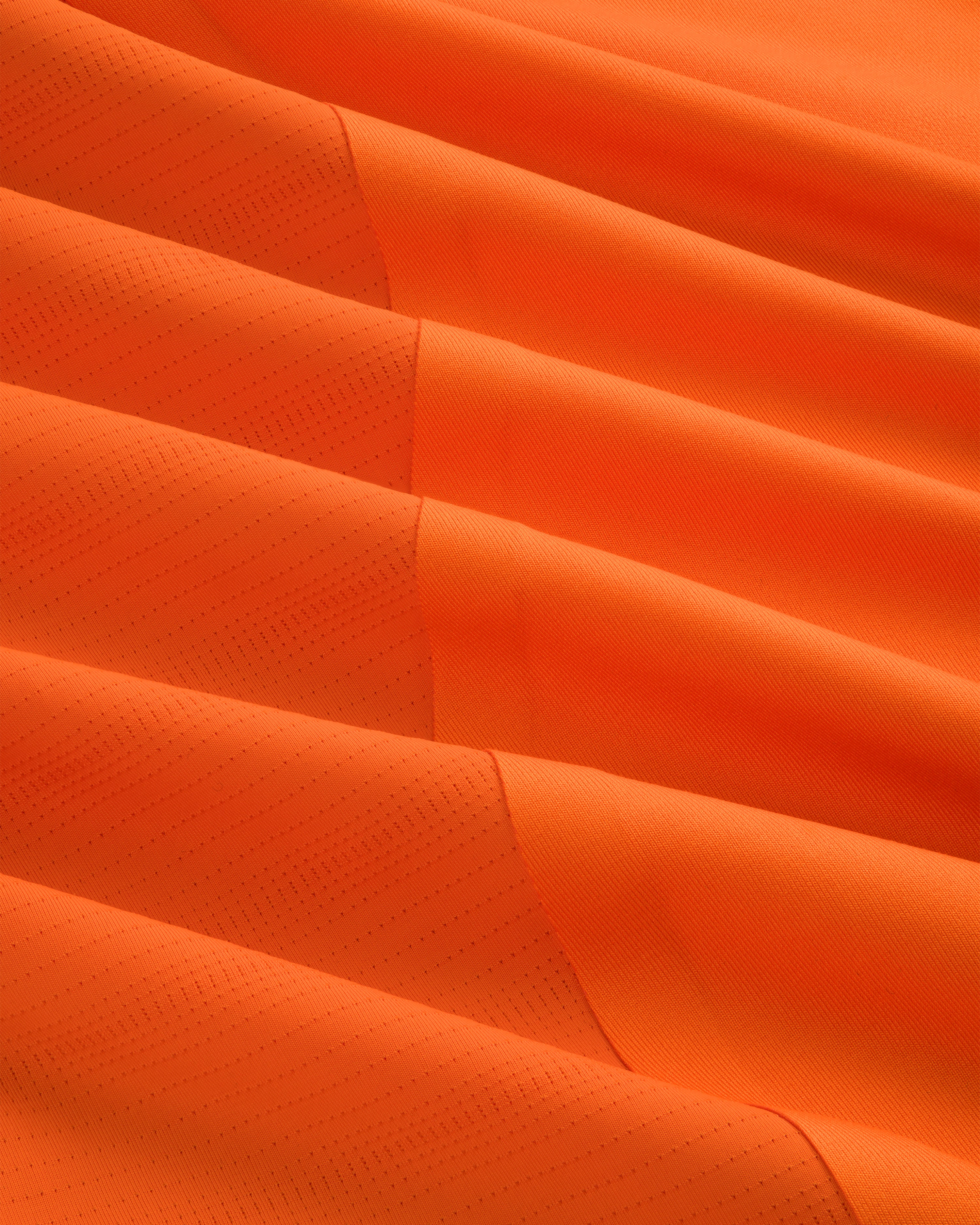 Close-up of ALD / New Balance Performance Long-Sleeve Tee in bright orange with subtle dotted texture and diagonal lines.