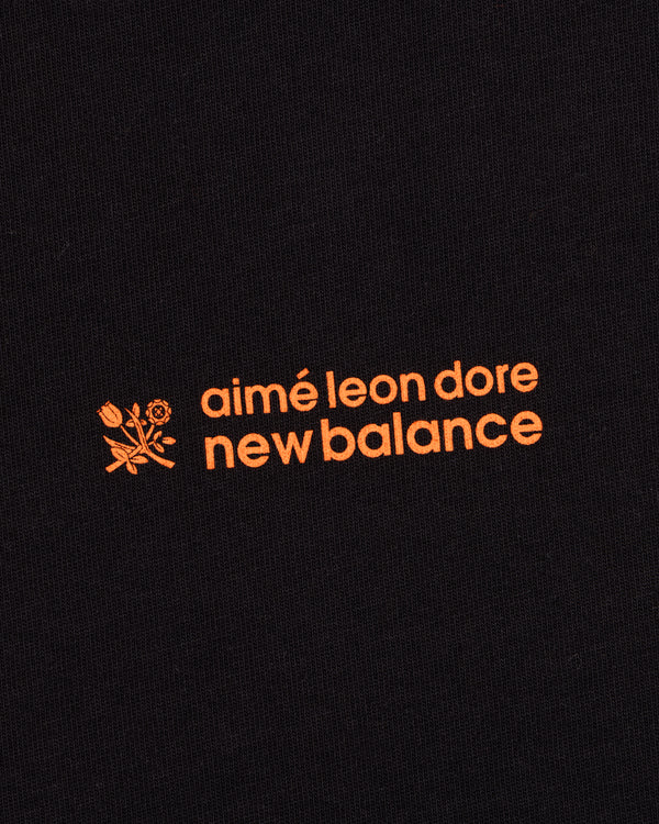 Black ALD / New Balance Running Bib Tee with orange text and a small floral graphic on black fabric.