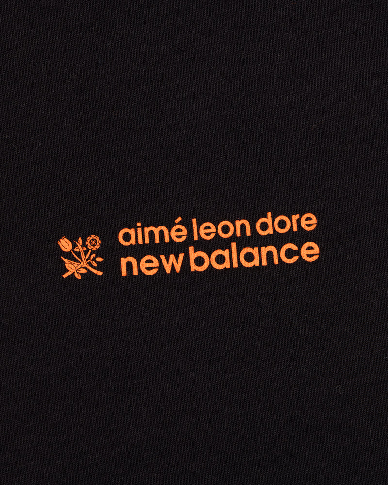 Black ALD / New Balance Running Bib Tee with orange text and a small floral graphic on black fabric.