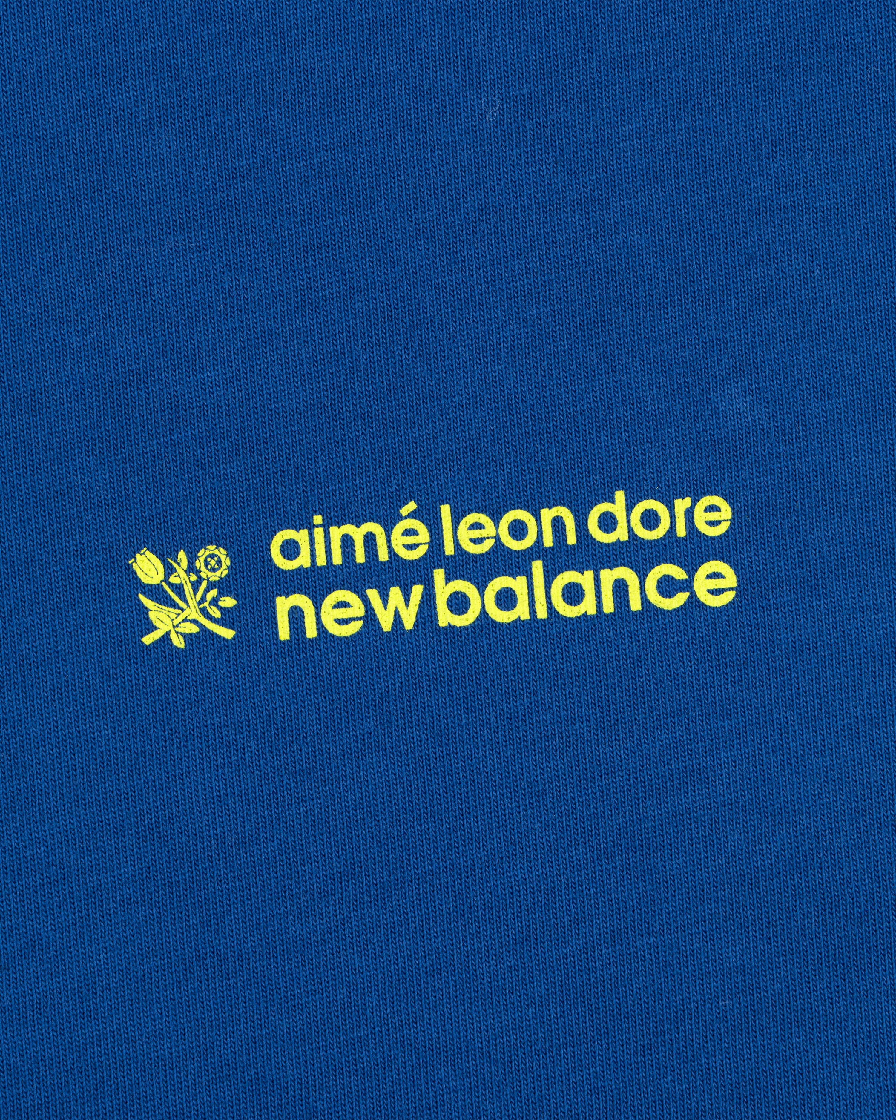 Yellow "ALD / New Balance Running Bib Tee" text and a small flower graphic on blue fabric.
