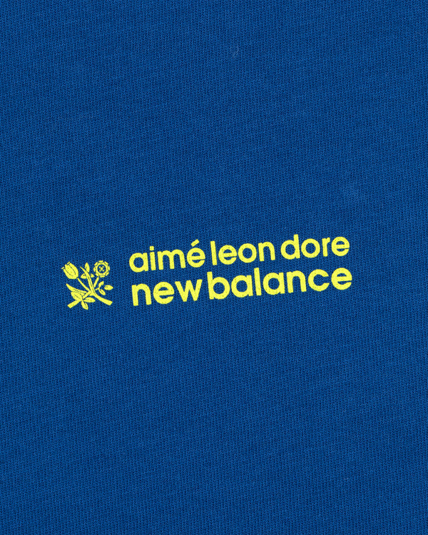 Yellow "ALD / New Balance Running Bib Tee" text and a small flower graphic on blue fabric.