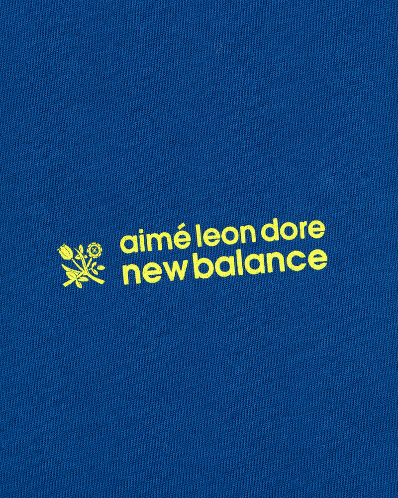 Yellow "ALD / New Balance Running Bib Tee" text and a small flower graphic on blue fabric.