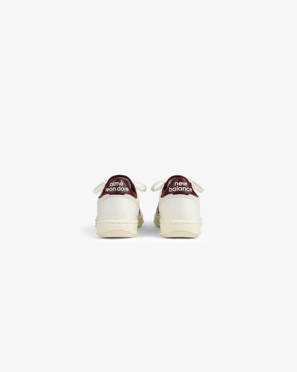 Back view of ALD / New Balance T500 Tennis Oxfords in off-white with dark red heel tabs featuring white text.