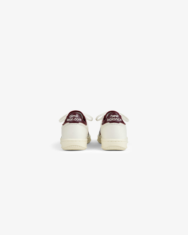 Back view of ALD / New Balance T500 Tennis Oxfords in off-white with dark red heel tabs featuring white text.