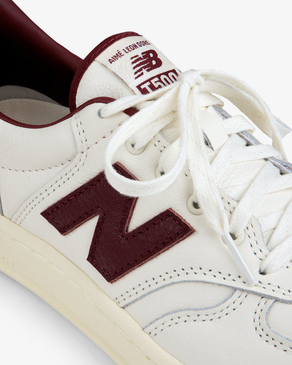 Off-white ALD / New Balance T500 Tennis Oxfords with a dark red logo, interior lining, and tongue patch.