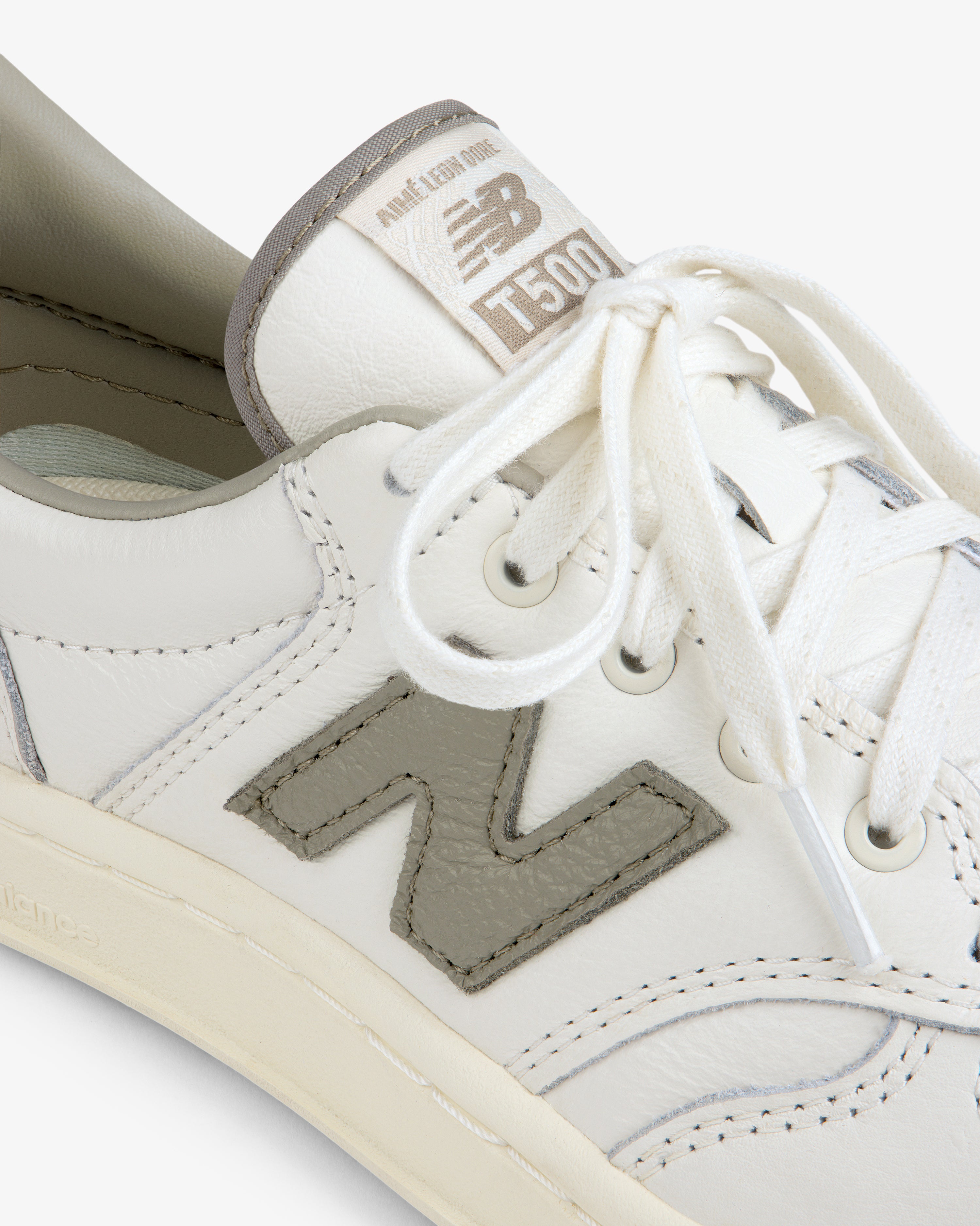 Close-up of a cream-colored ALD / New Balance T500 Tennis Oxford with a grey N logo and matching grey tongue label.