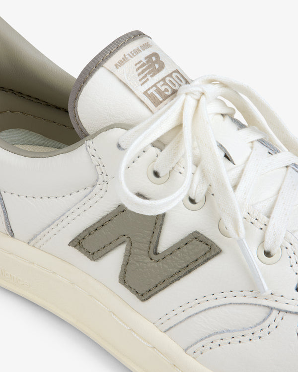 Close-up of a cream-colored ALD / New Balance T500 Tennis Oxford with a grey N logo and matching grey tongue label.