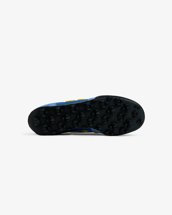 Bottom view of an ALD / New Balance Gator sneaker with a blue upper and a black, cleated rubber sole.
