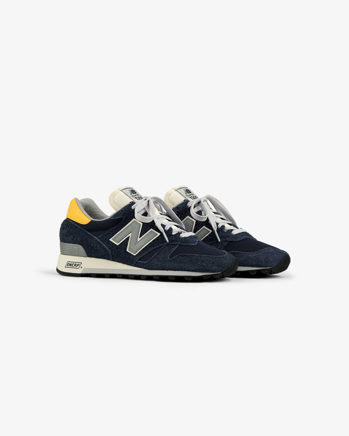 A pair of ALD / New Balance Made in USA 1300 navy blue sneakers with white laces and a yellow heel accent.