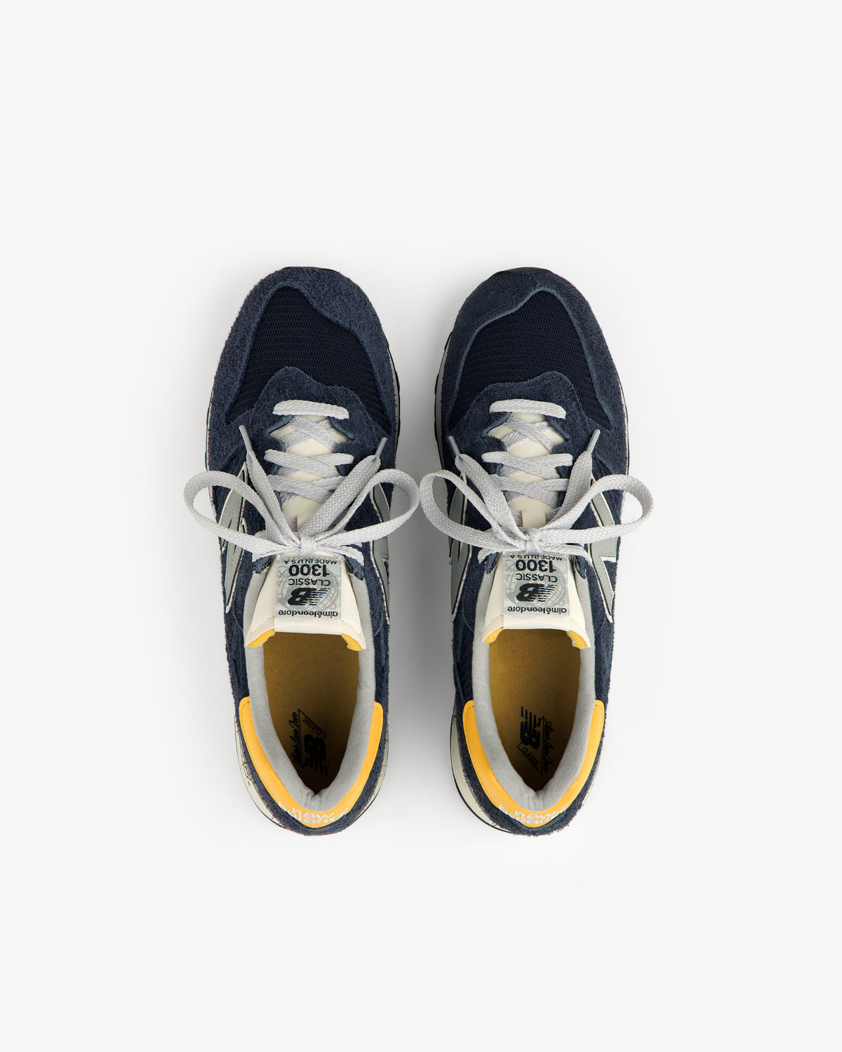 ALD / New Balance Made in USA 1300 sneakers in navy, white, and yellow accents, top view on white background.