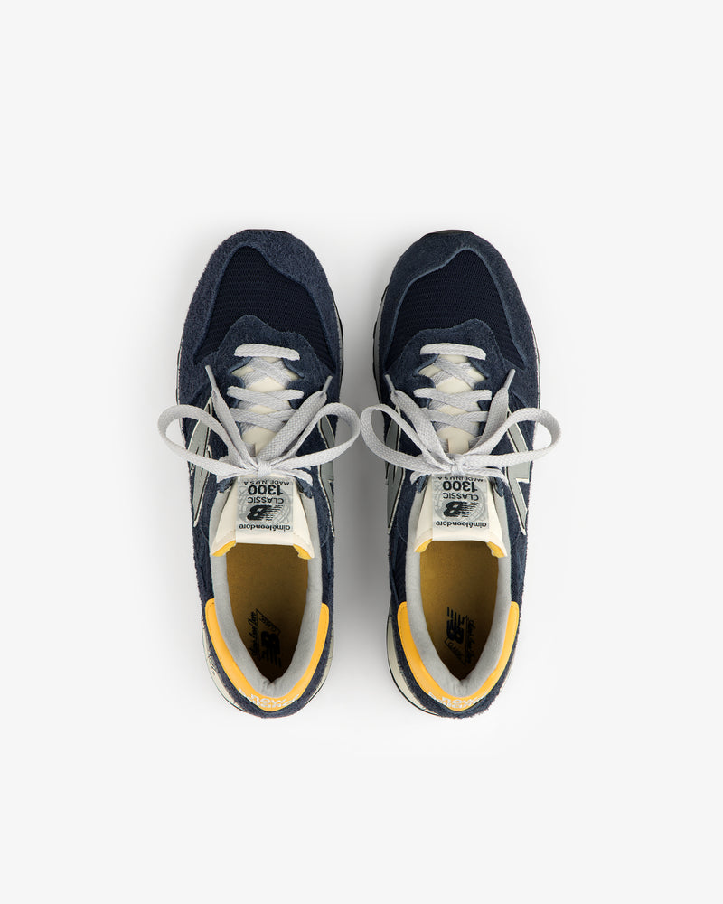 ALD / New Balance Made in USA 1300 sneakers in navy, white, and yellow accents, top view on white background.
