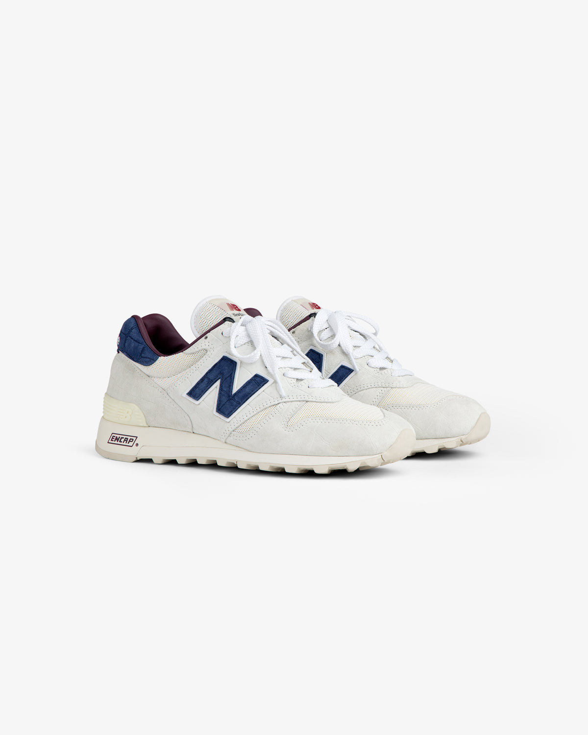 New Balance Made in USA 1300 sneakers in white with navy accents, white laces, and cream soles on a white background.