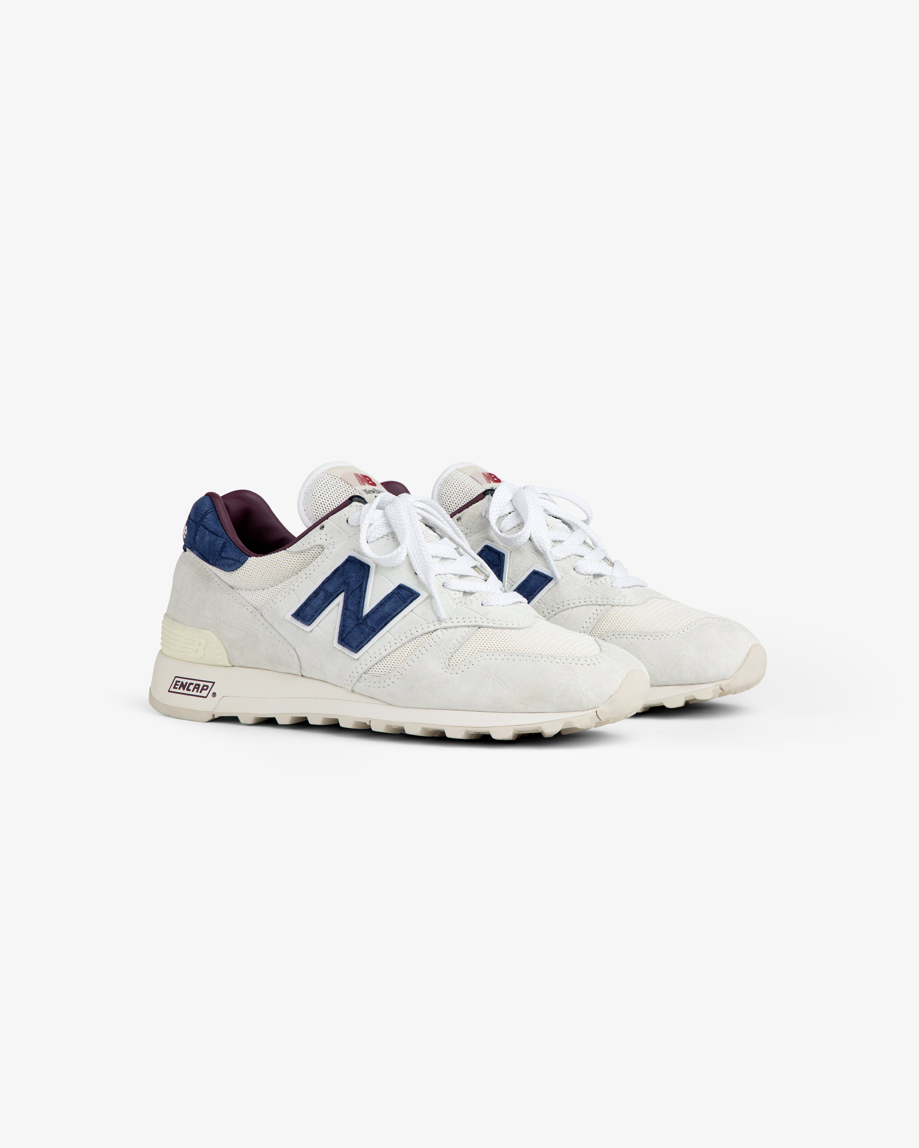New Balance Made in USA 1300 sneakers in white with navy accents, white laces, and cream soles on a white background.