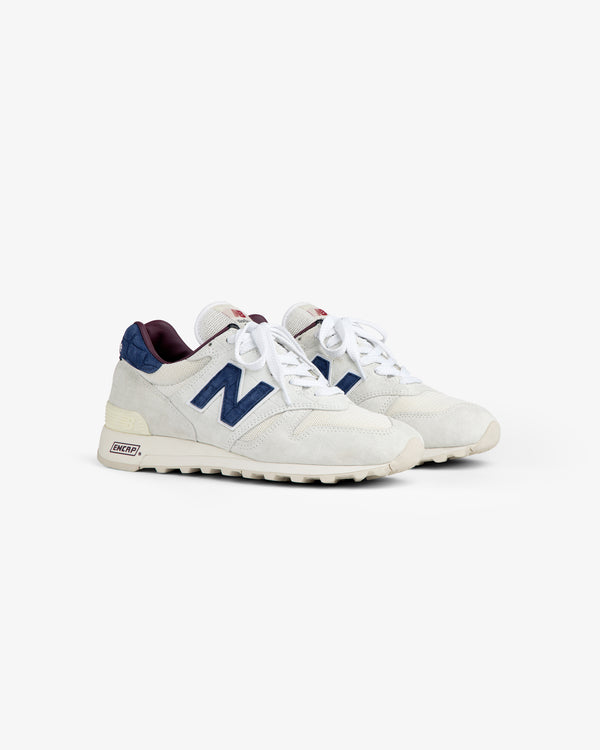 New Balance Made in USA 1300 sneakers in white with navy accents, white laces, and cream soles on a white background.