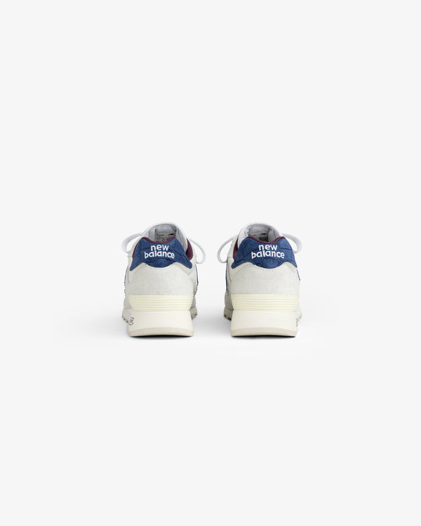 Rear view of New Balance Made in USA 1300 sneakers, blue/gray uppers, white soles, on a white background.