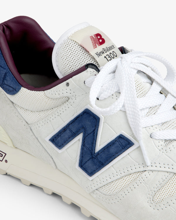 Close-up of a white New Balance Made in USA 1300 with blue logo, maroon lining, and white laces.