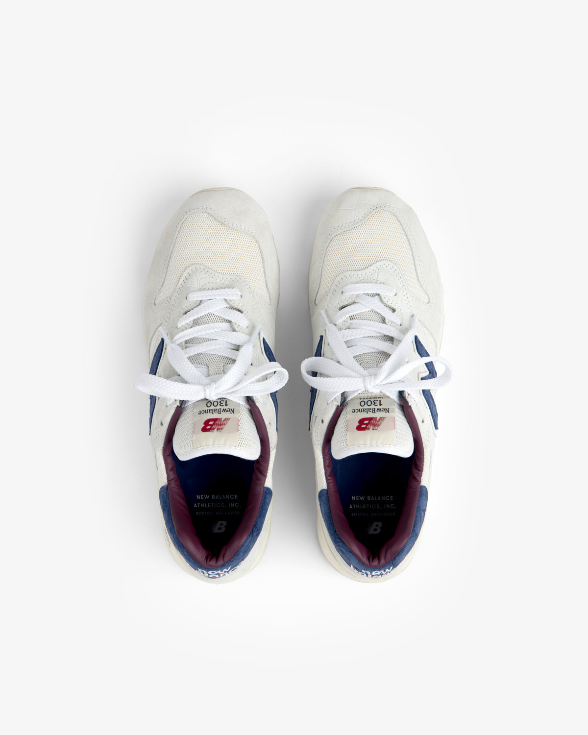 New Balance Made in USA 1300 sneakers in white with blue and maroon accents, top view on a white background.