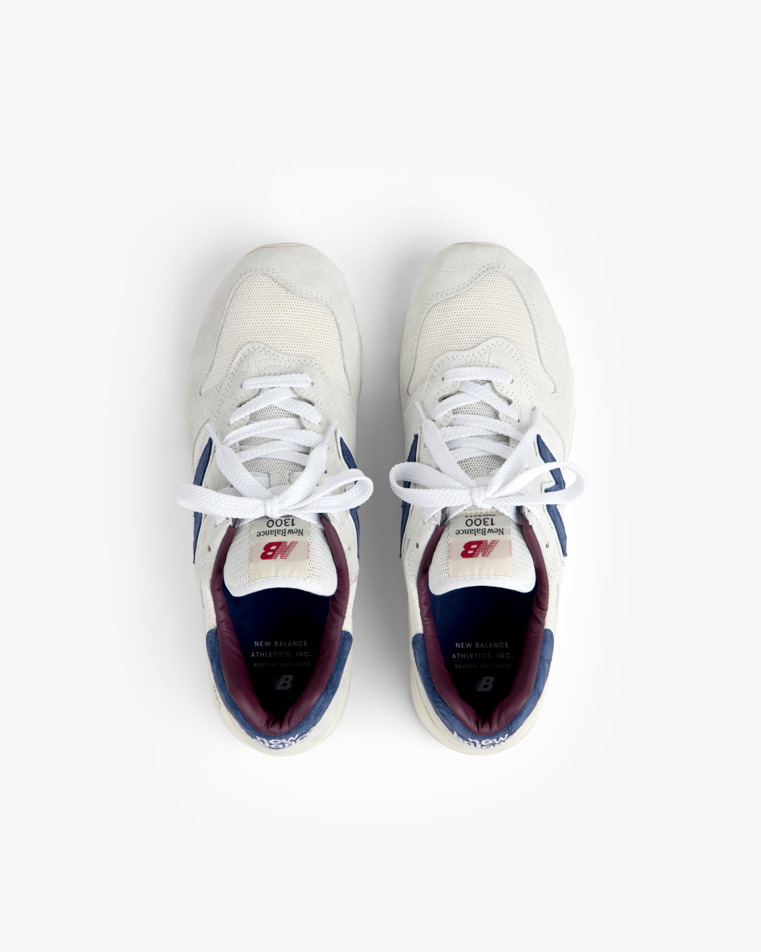 New Balance Made in USA 1300 sneakers in white with blue and maroon accents, top view on a white background.