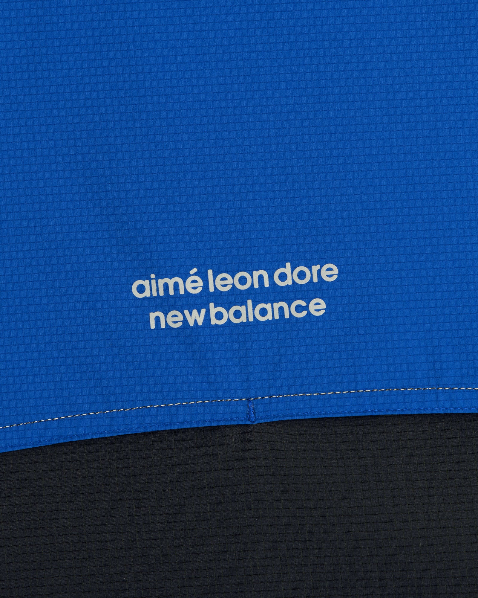 Close-up of blue ALD / New Balance Performance Nylon Jacket with white text above a seam.