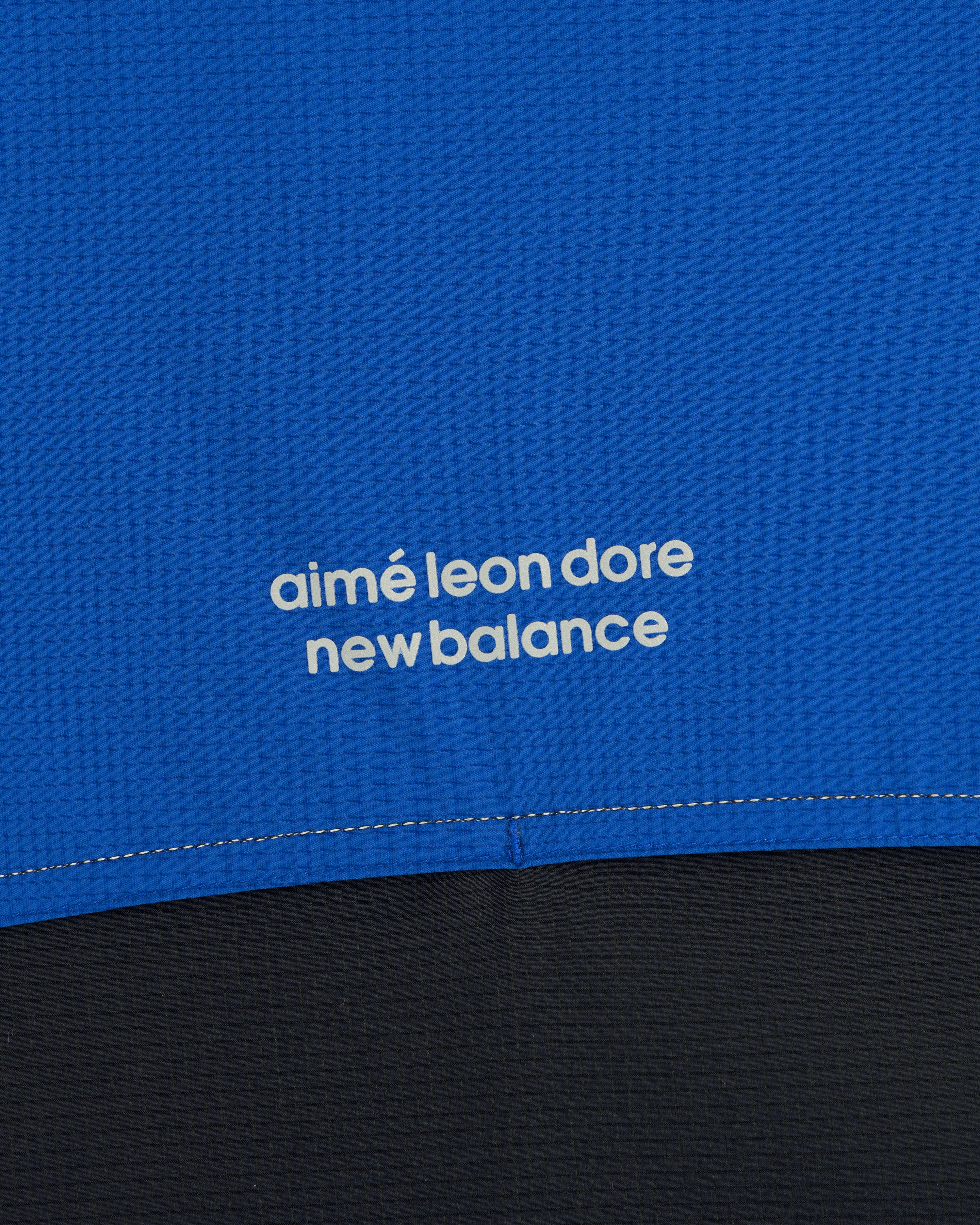 Close-up of blue ALD / New Balance Performance Nylon Jacket with white text above a seam.