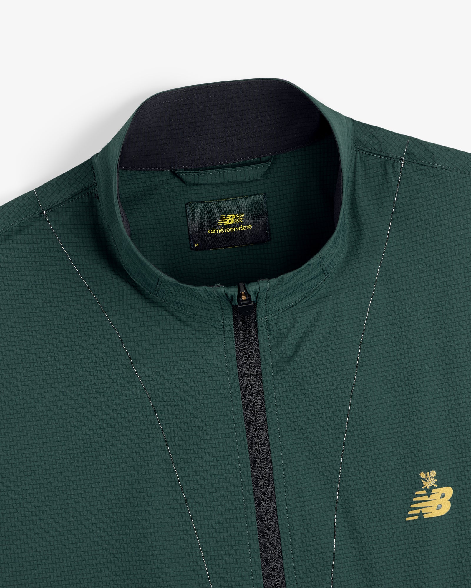 Close-up of a green ALD / New Balance Performance Nylon Jacket with zip front and gold chest logo.