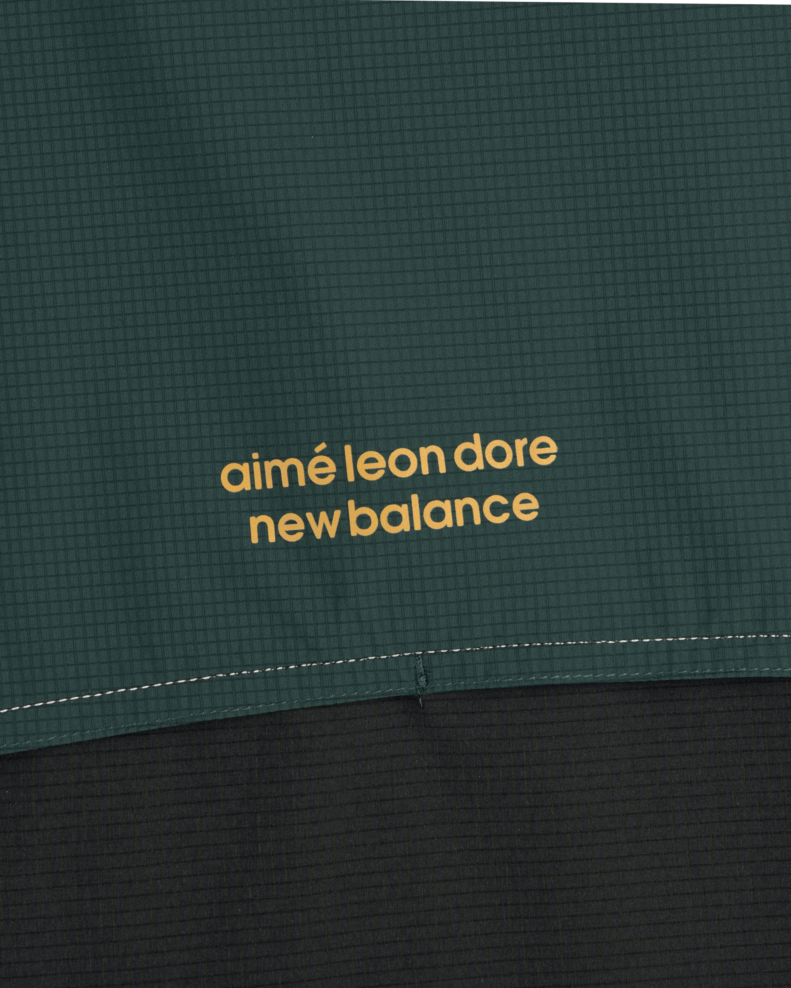 Close-up of green and black ALD / New Balance Performance Nylon Jacket with yellow printed text.