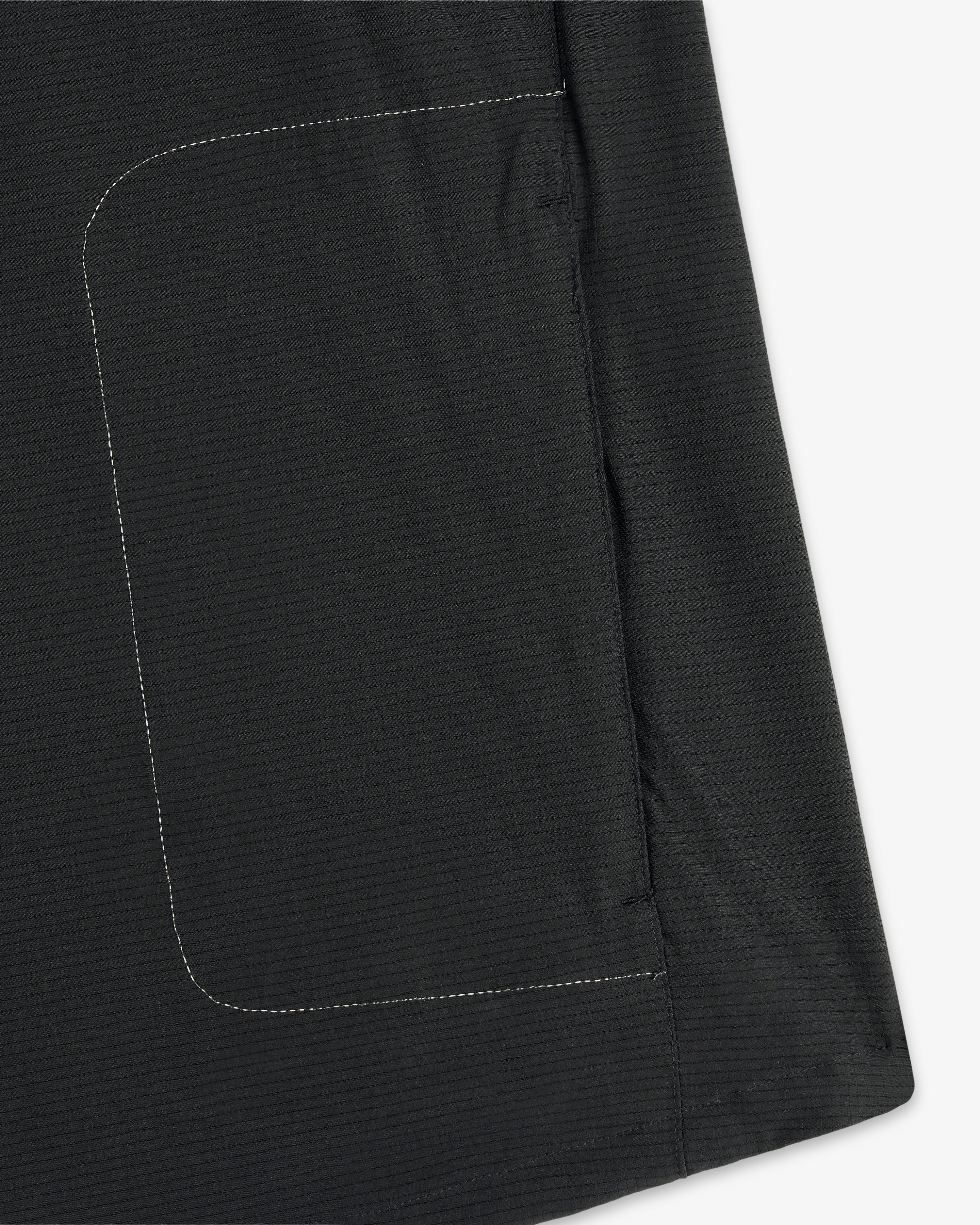 Close-up of the ALD / New Balance Performance Nylon Jacket showing a black fabric, rectangular pocket, and white stitching.